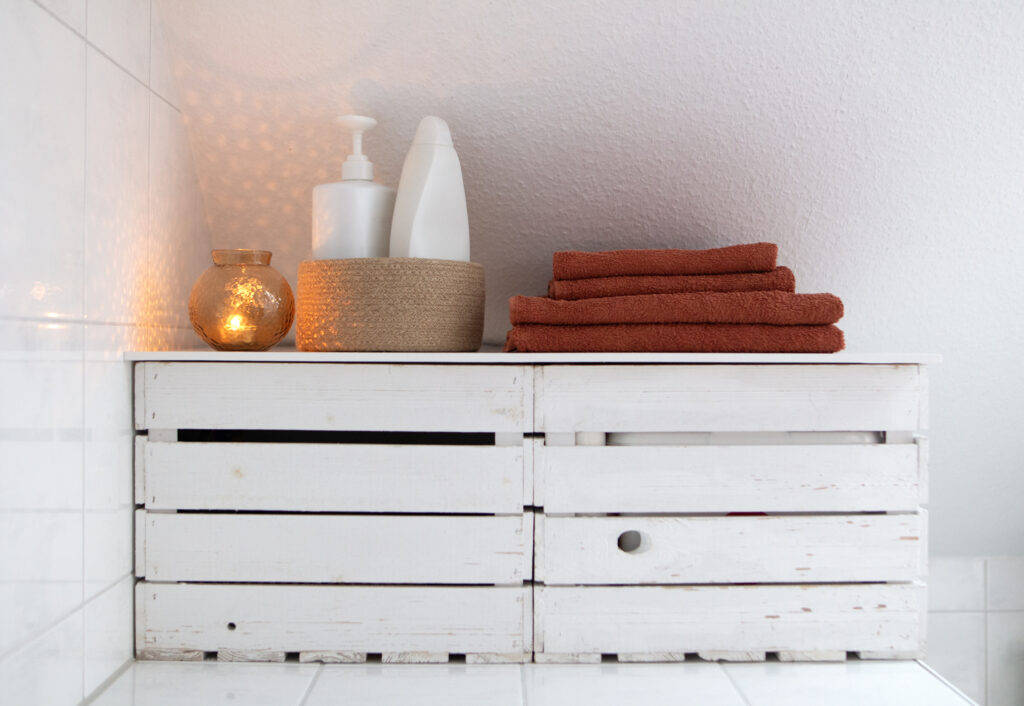 Foto von Badezimmer, 2 Holzboxen zur aufbewarung, darauf rostrote Handtücher, Duschgel und eine brennende Kerze - für Feng-Shui